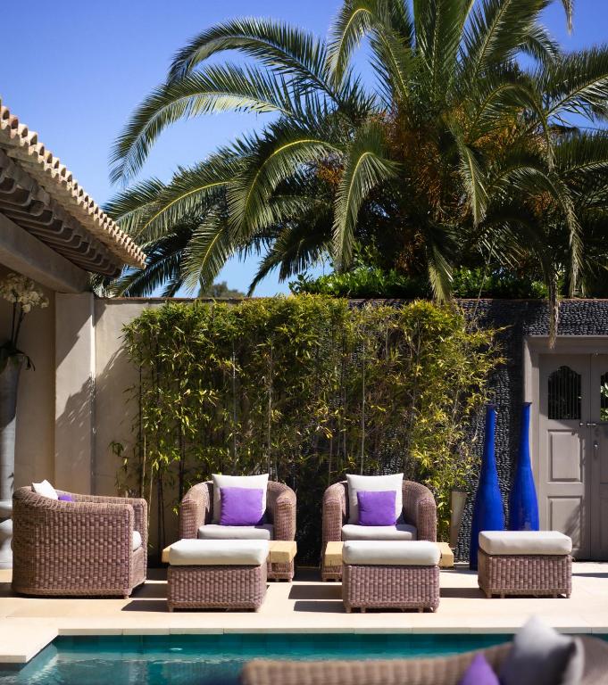 a patio with two chairs and a pool with purple pillows at Le Pre de la Mer in Saint-Tropez