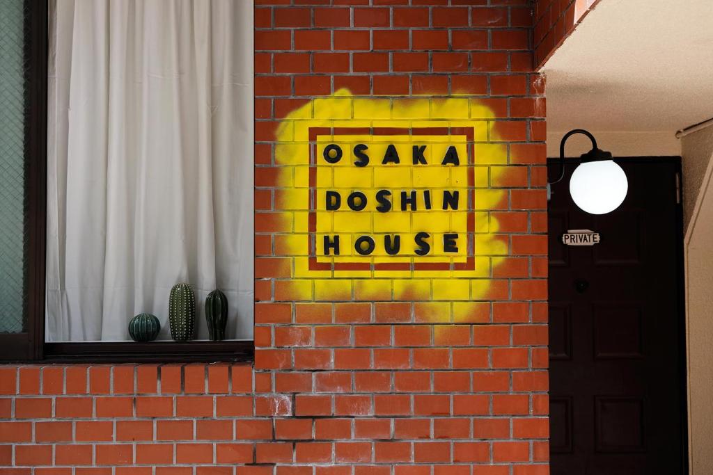 ein gelbes Schild an der Seite einer Ziegelmauer in der Unterkunft OSAKA DOSHIN HOUSE in Osaka