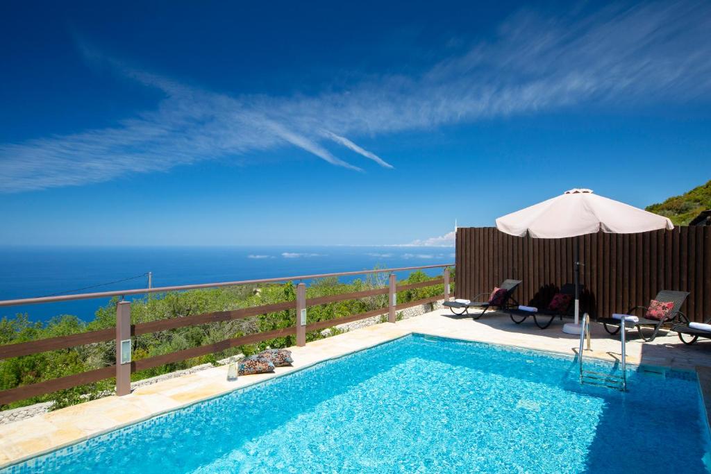 a swimming pool with an umbrella and a view of the ocean at Amadryades Villas in Chortáta