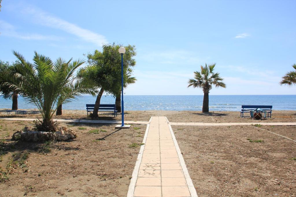 a walkway on the beach with two benches and palm trees at Demetris apartment in Meneou