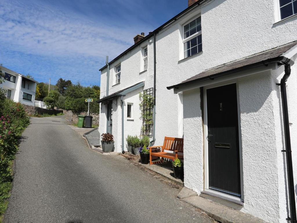 a white house with a door and a bench on a street at Bryn Teg Cottage in Menai Bridge