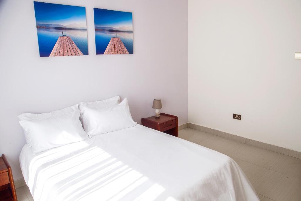 a bedroom with a white bed with two pictures on the wall at MC Apartments in Lusaka
