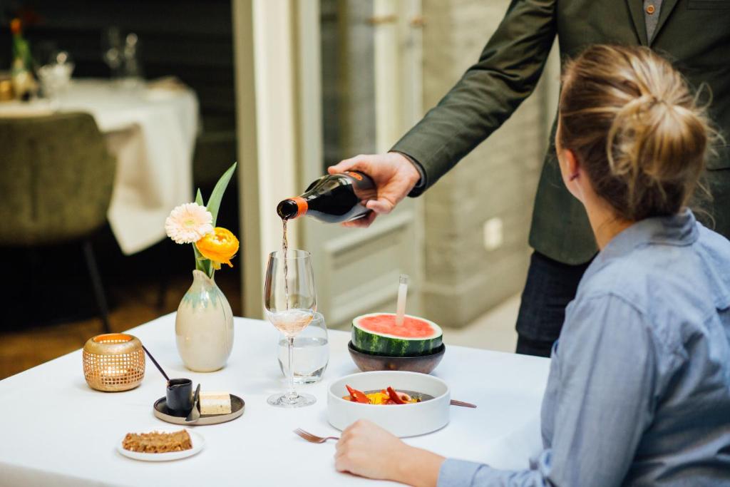 a woman sitting at a table with a person pouring a drink at Hotel ML in Haarlem