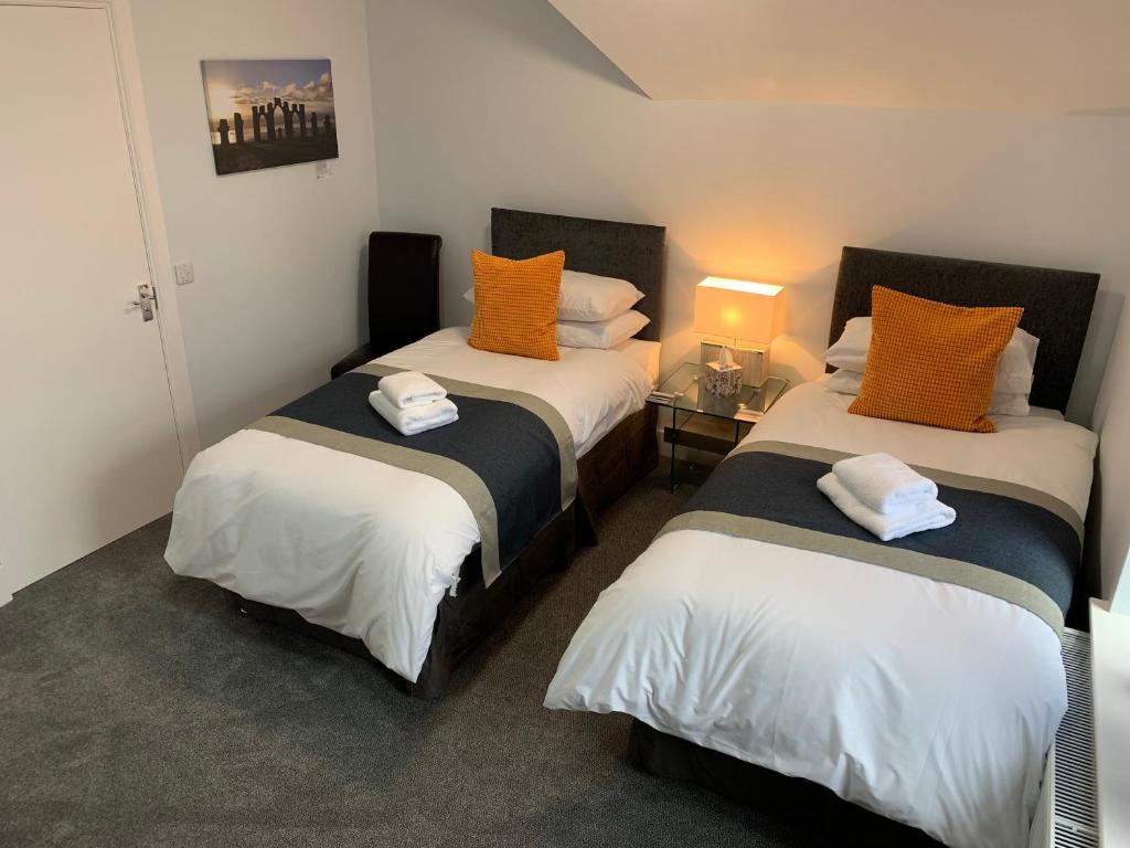 a bedroom with two beds with orange and white pillows at Muir Bank in Muir of Ord