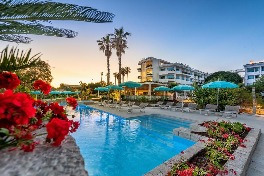 una piscina in un resort con fiori rossi e ombrelloni blu di Acacia Palace a Marina di Ragusa