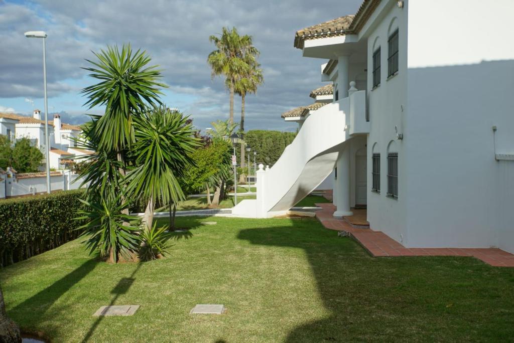 un patio con palmeras y una casa blanca en LA BARROSA-NOVO SANCTI PETRI, wifi, aire acondicionado, parking, en Chiclana de la Frontera