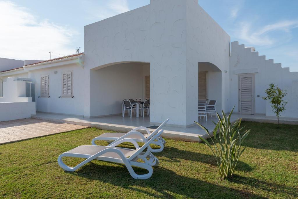 a white house with two lounge chairs in the yard at Blue Sea Villas by Wonderful Italy in Ostuni