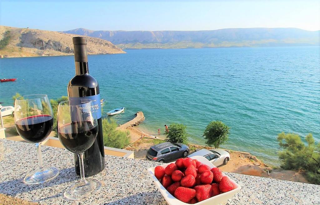 una botella de vino y un tazón de fresas sobre una mesa en Apartments Niko Metajna, island Pag, en Metajna