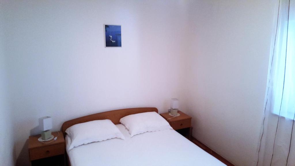 a bedroom with a white bed and two nightstands with two lamps at Apartments Niko Metajna, island Pag in Metajna