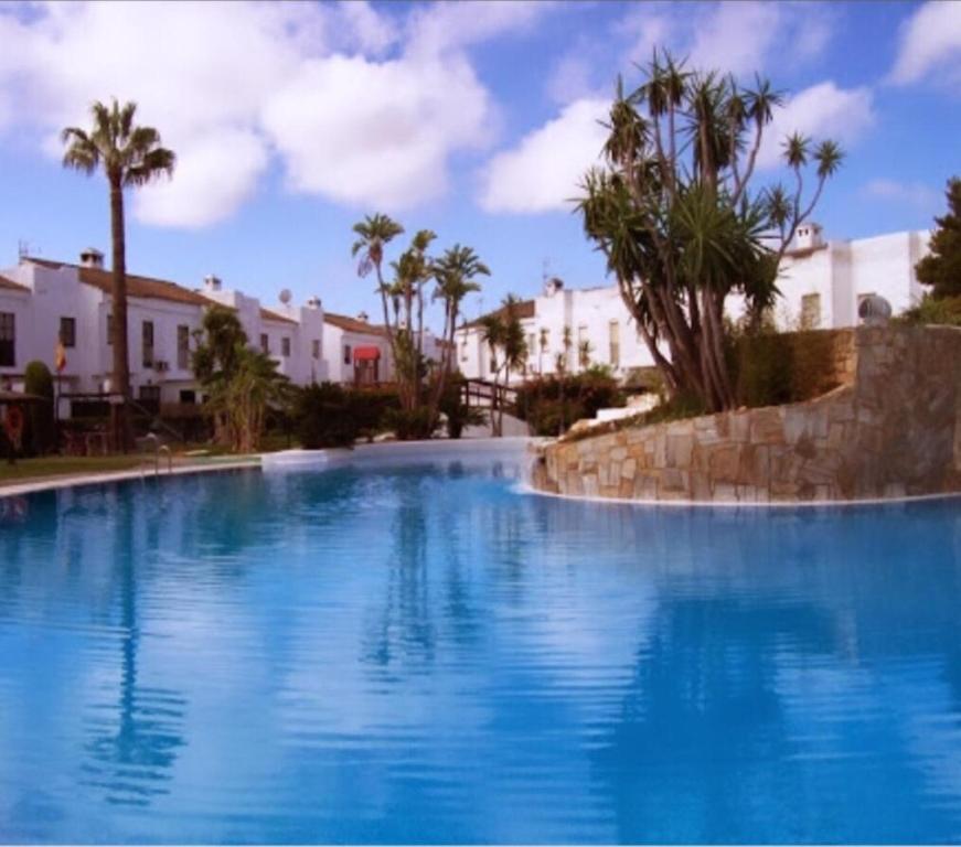 a large blue swimming pool with palm trees and buildings at Real de la Barrosa in Chiclana de la Frontera