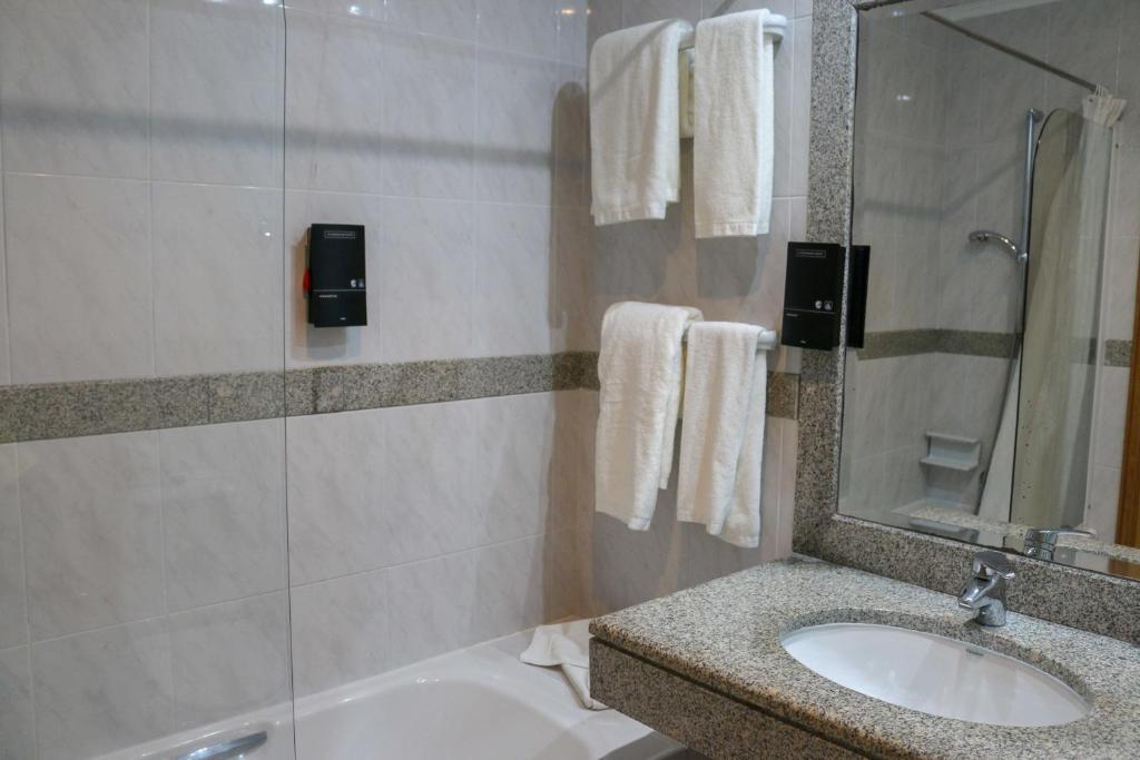 a bathroom with a sink and a tub and a mirror at Hotel Horta in Horta