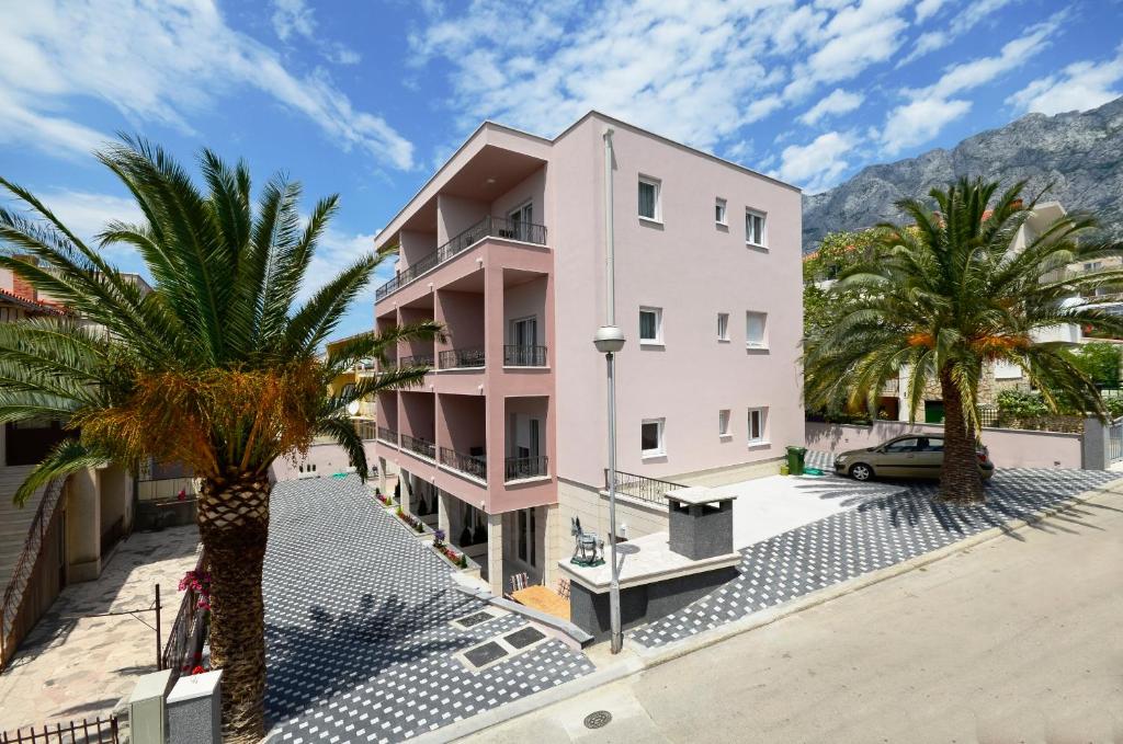 a pink building with palm trees in front of it at Villa Cavar, Apartments Close to the Beach in Makarska