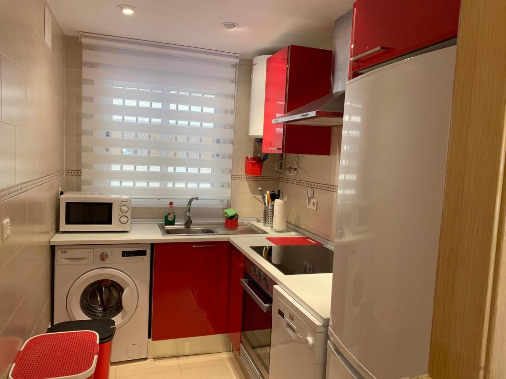 cocina con armarios rojos, fregadero y microondas en Apartamentos Marina Dor Agua Marina en Oropesa del Mar