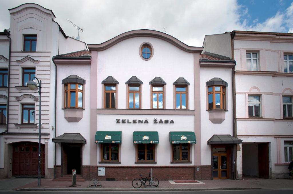 a white building with green awnings on a street at Penzion Zelená Žába in Pardubice