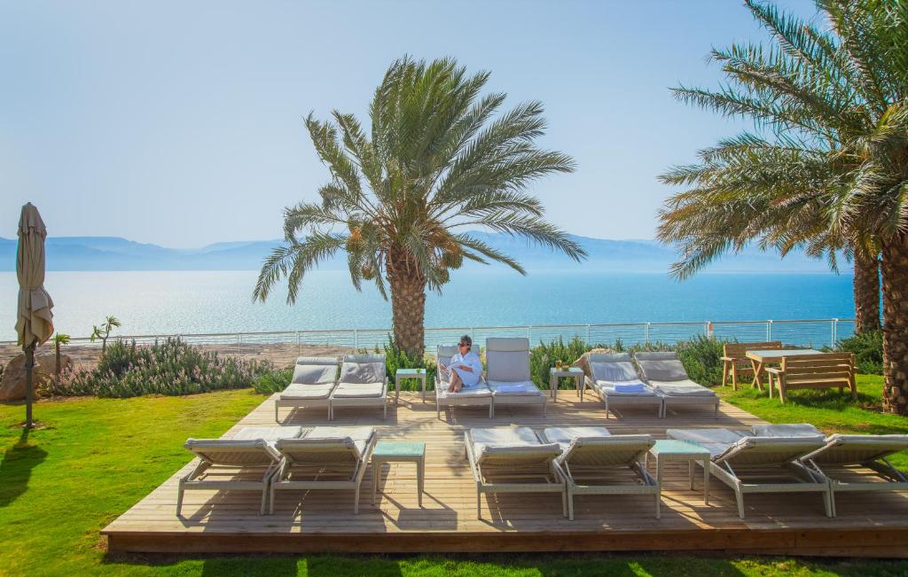 una persona sentada en una terraza con sillas y el océano en Ein Gedi Kibbutz Hotel, en Ein Gedi