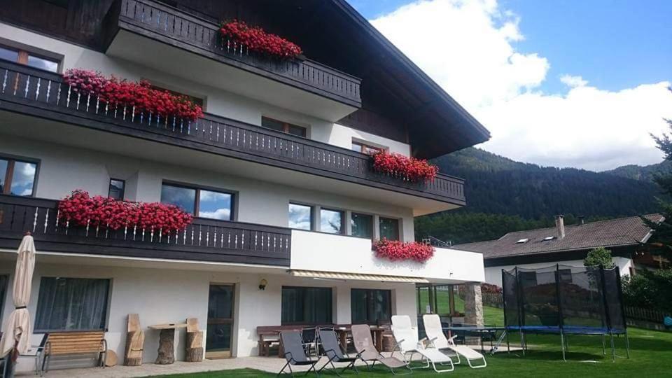 a building with chairs and red flowers on the balcony at Pension Tirol in San Valentino alla Muta