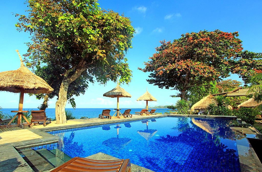 una piscina con sillas y sombrillas junto al océano en Sunsethouse Lombok, en Senggigi 