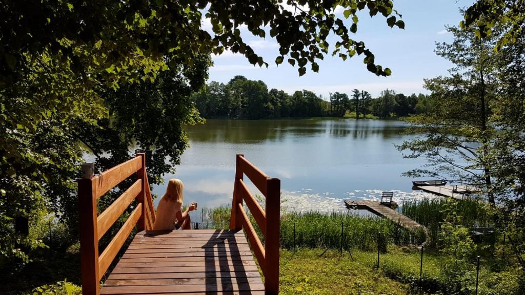 a woman sitting on a wooden bridge near a lake at Urocza Przystan in Kiemiany