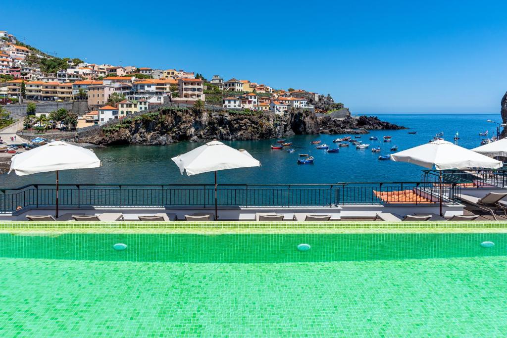 a swimming pool with umbrellas and boats in the water at Pestana Churchill Bay in Câmara de Lobos