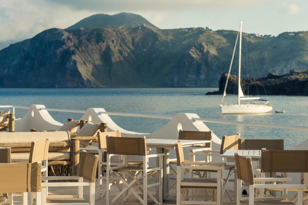 a group of tables and chairs next to the water with a boat at Mari del Sud Resort in Vulcano