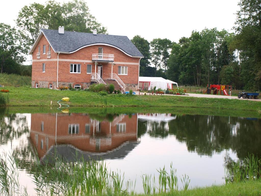 Una gran casa de ladrillo rojo se refleja en un estanque en Guest House Kalnu pūpoli, en Šengeida