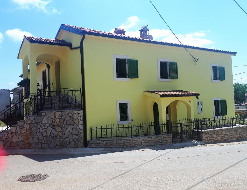 a yellow house with green shutters and a fence at Apartment Aurora in Kaštelir
