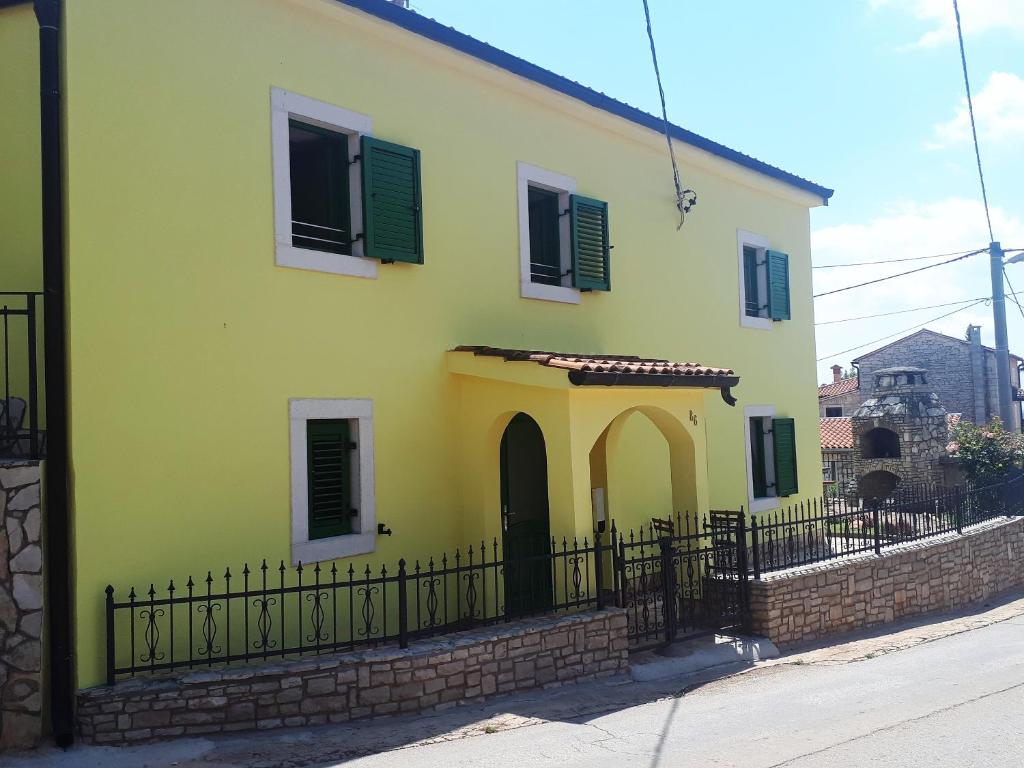 una casa amarilla y verde con una valla negra en Apartment Terra Rossa, en Kaštelir