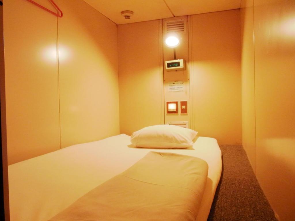 um pequeno quarto com uma cama branca num quarto em Capsule Hotel Block Room em Tóquio