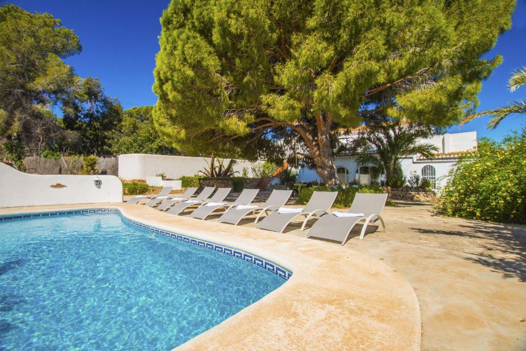 a pool with lounge chairs and trees and a house at Villa Fanadix - Plusholidays in Benissa