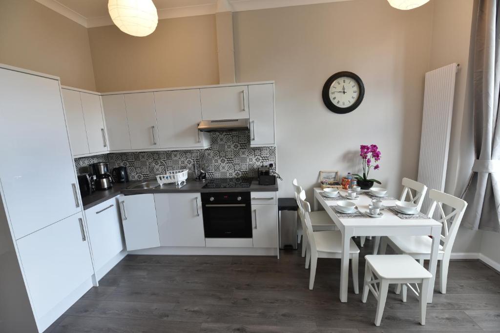 une cuisine avec des placards blancs et une table avec des chaises dans l'établissement Pleasance Apartment Ground Floor Main Door Access, à Édimbourg