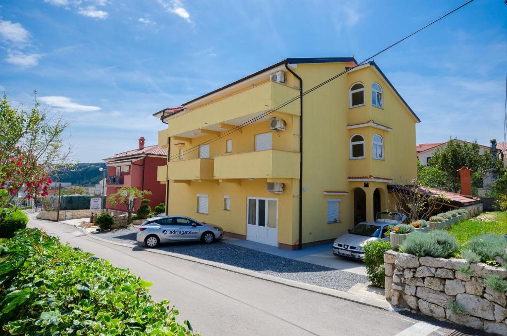 uma casa amarela com dois carros estacionados numa garagem em Apartments Mirjana em Lopar