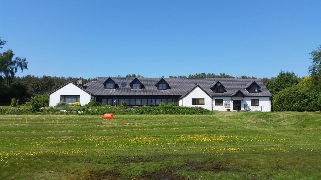une maison blanche avec un toit noir dans un champ dans l'établissement Delny Muir House, à Invergordon
