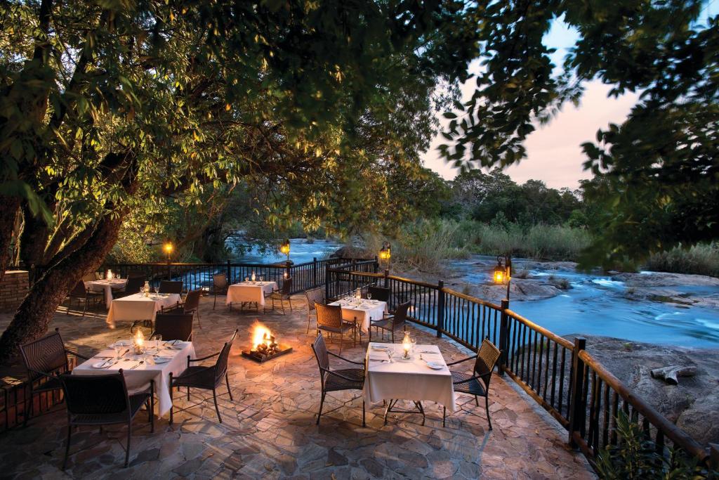 a patio with tables and chairs next to a river at Kruger Park Lodge in Hazyview