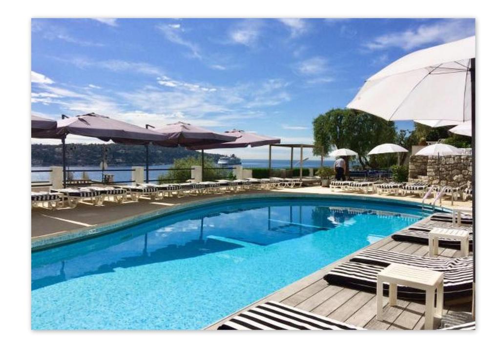 a large swimming pool with chairs and umbrellas at Hôtel Le Versailles in Villefranche-sur-Mer