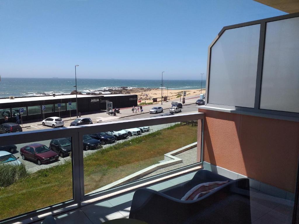 uma varanda com vista para um parque de estacionamento e para o oceano em H2OPorto Beachfront Apartment em Vila Nova de Gaia