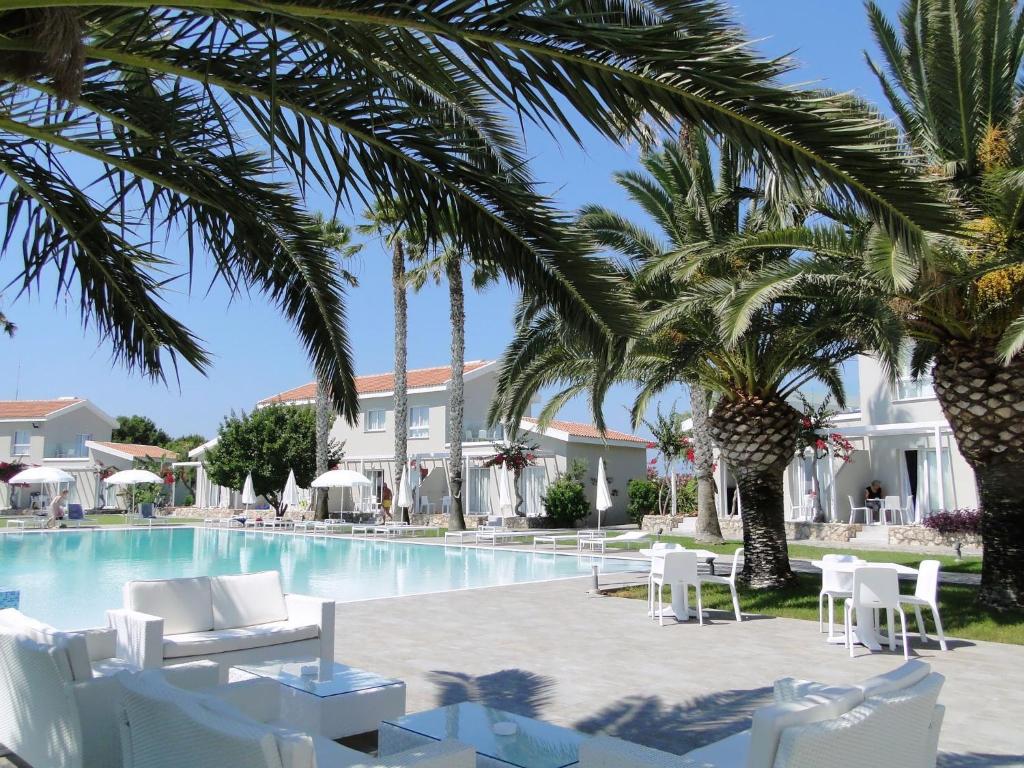 a resort pool with white chairs and palm trees at Mon Repos Hotel in Ayia Napa