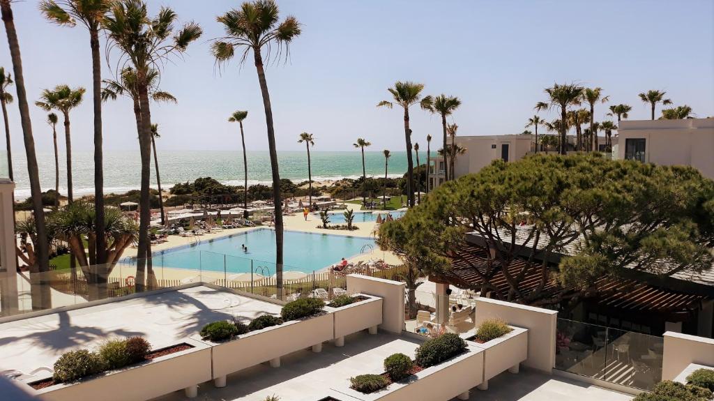 a view of a pool with palm trees and the ocean at Hipotels Barrosa Park in Chiclana de la Frontera