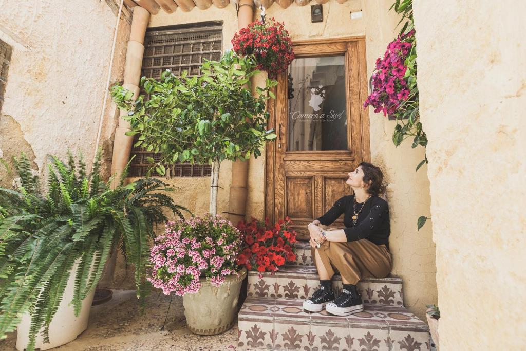 une femme assise sur les marches d'un immeuble fleuri dans l'établissement Camere a Sud, à Agrigente