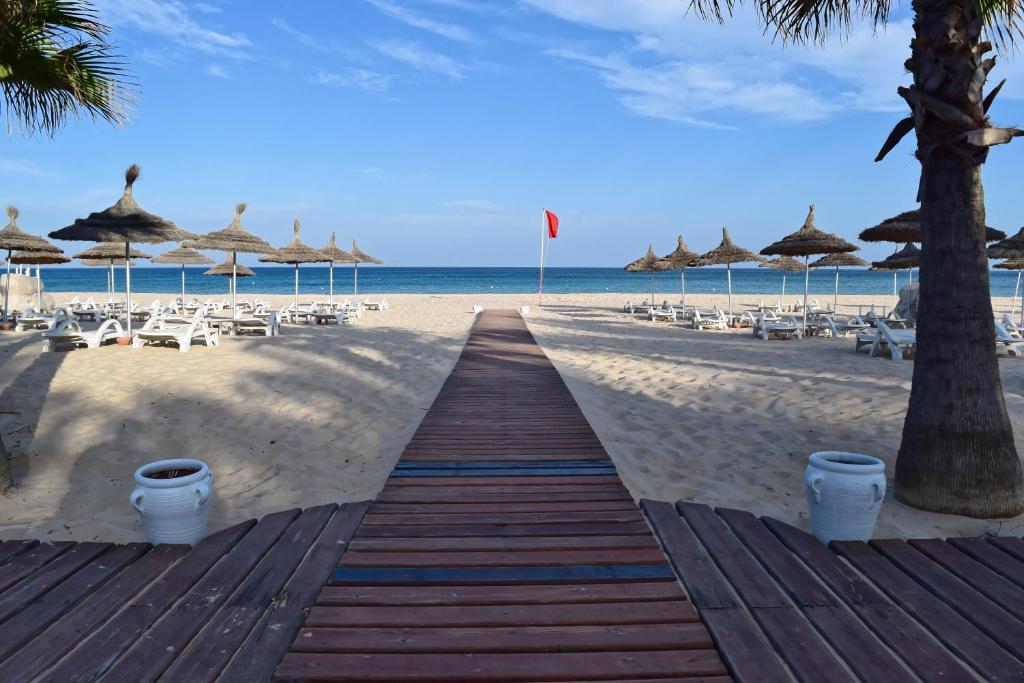 a boardwalk on the beach with chairs and umbrellas at OCEANA Hotel & Spa in Hammamet