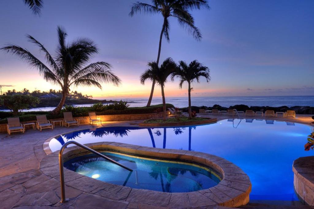 una piscina en un complejo con palmeras y el océano en Whalers Cove in Poipu, en Koloa