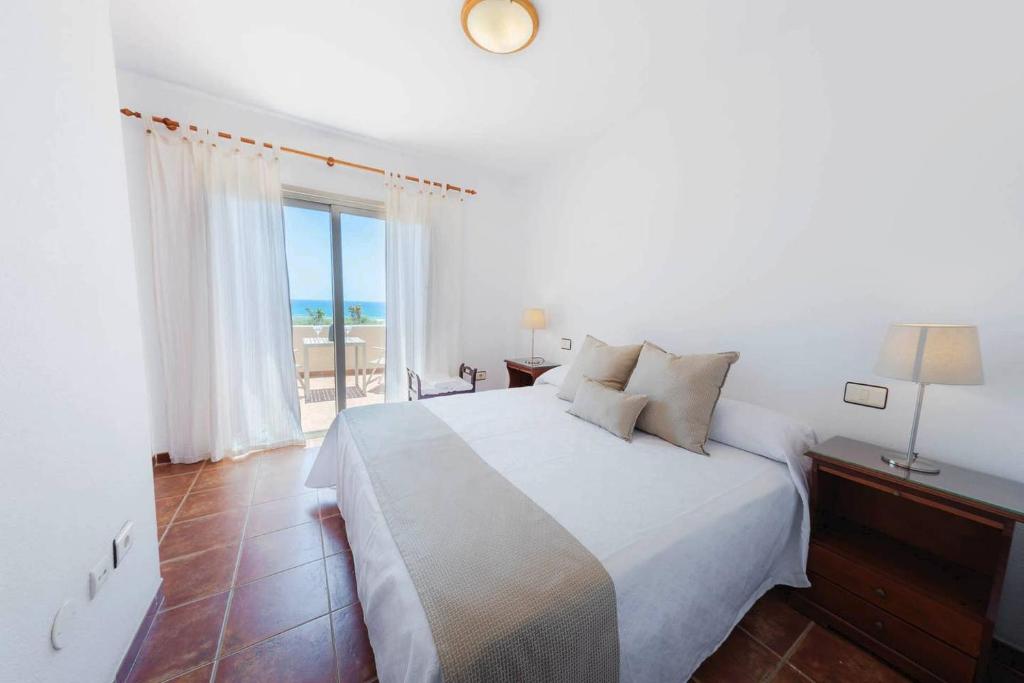 ein weißes Schlafzimmer mit einem Bett und einem großen Fenster in der Unterkunft Luminoso adosado frente al mar in El Médano