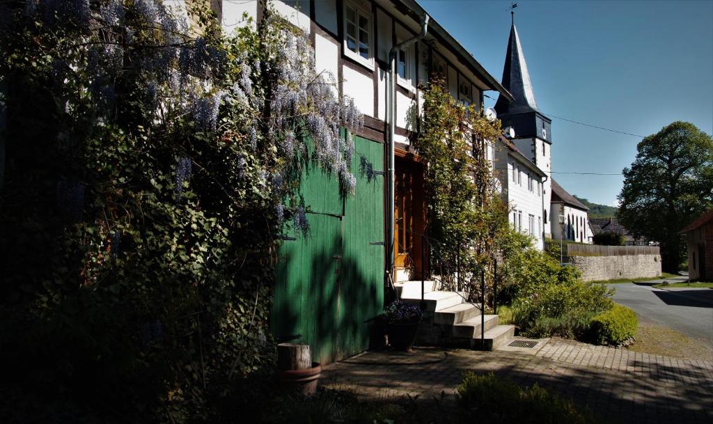 ein mit Efeu bedecktes Gebäude mit einer grünen Tür und einer Kirche in der Unterkunft Heidschnuckenhof in Niedermeiser