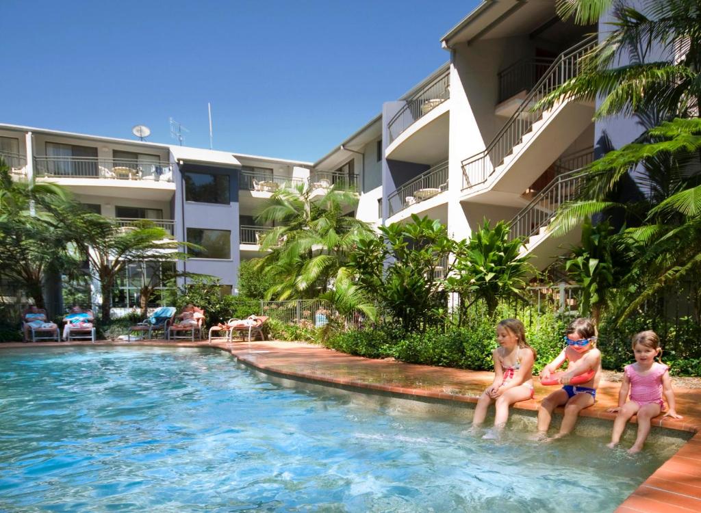 3 niños sentados en la piscina de un complejo en Flynns Beach Resort, en Port Macquarie