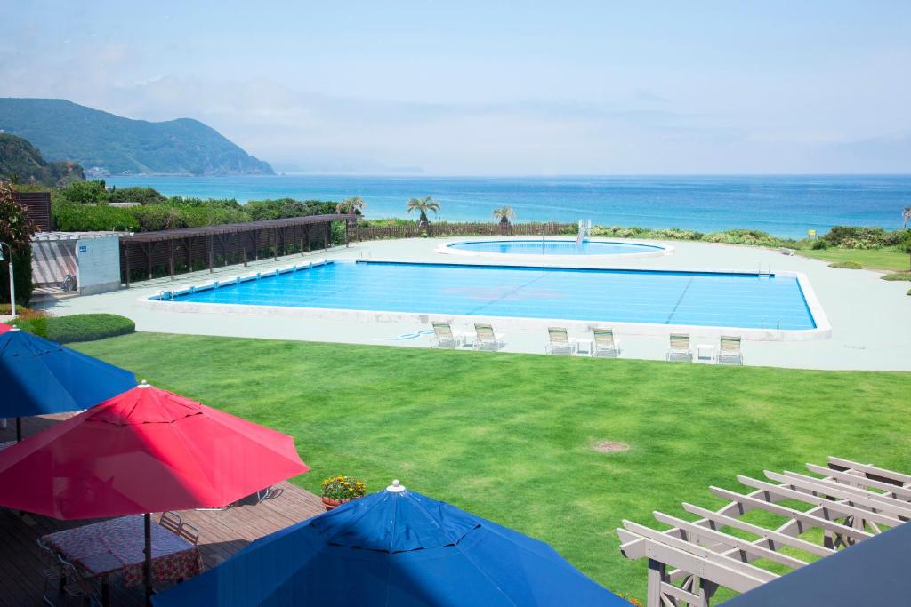 a swimming pool with chairs and umbrellas and the ocean at Hotel Izukyu in Shimoda