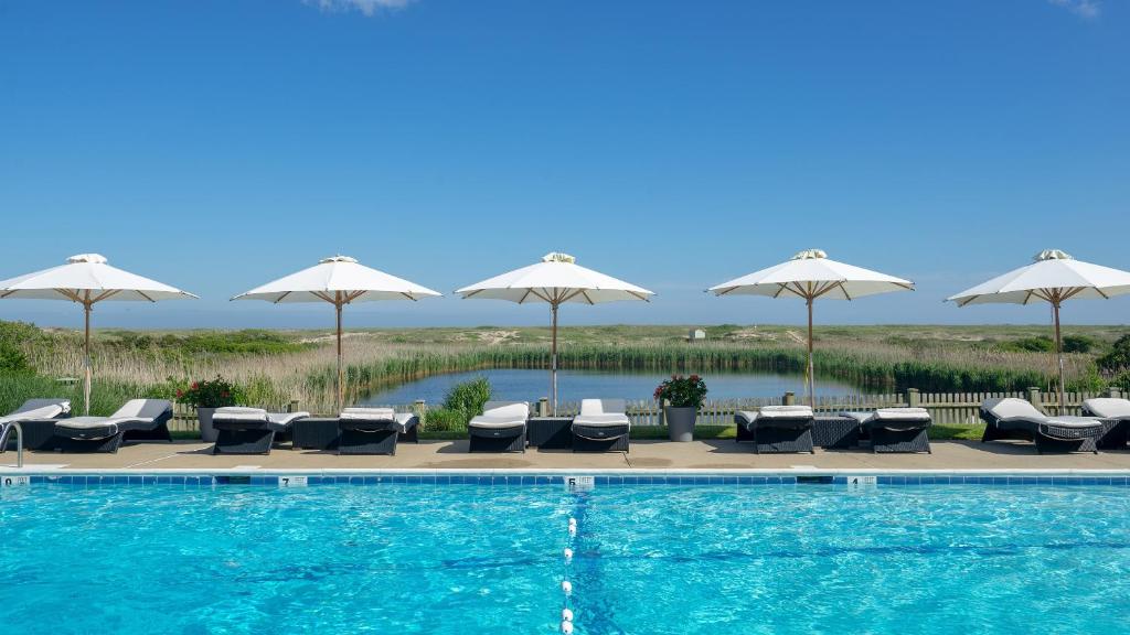 a swimming pool with lounge chairs and umbrellas at The Ocean Dunes at Amagansett in Amagansett