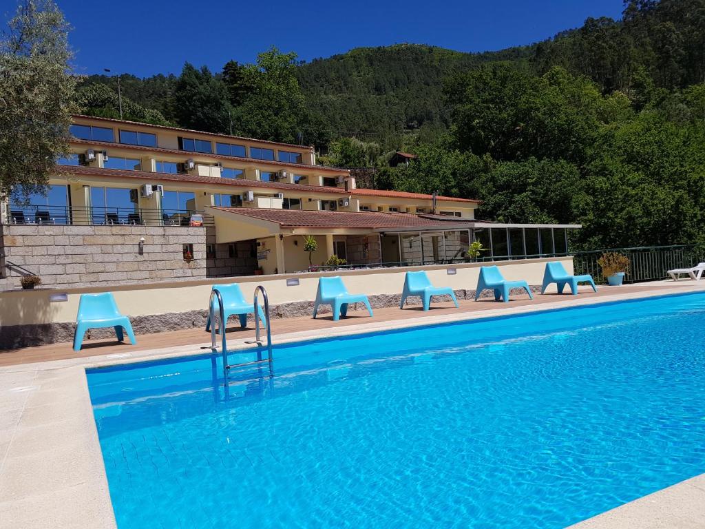 uma piscina com cadeiras azuis ao lado de um edifício em Hotel Lagoa Azul do Geres no Gerês
