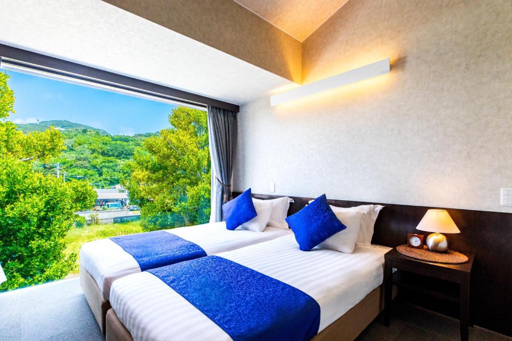 two beds in a room with a large window at Kerama Terrace in Tokashiki