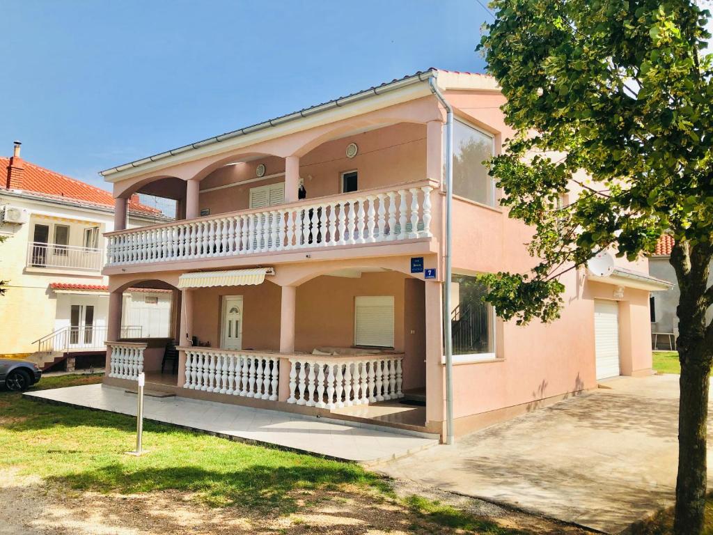 różowy dom z balkonem i drzewem w obiekcie Apartmani Apolon w mieście Starigrad-Paklenica