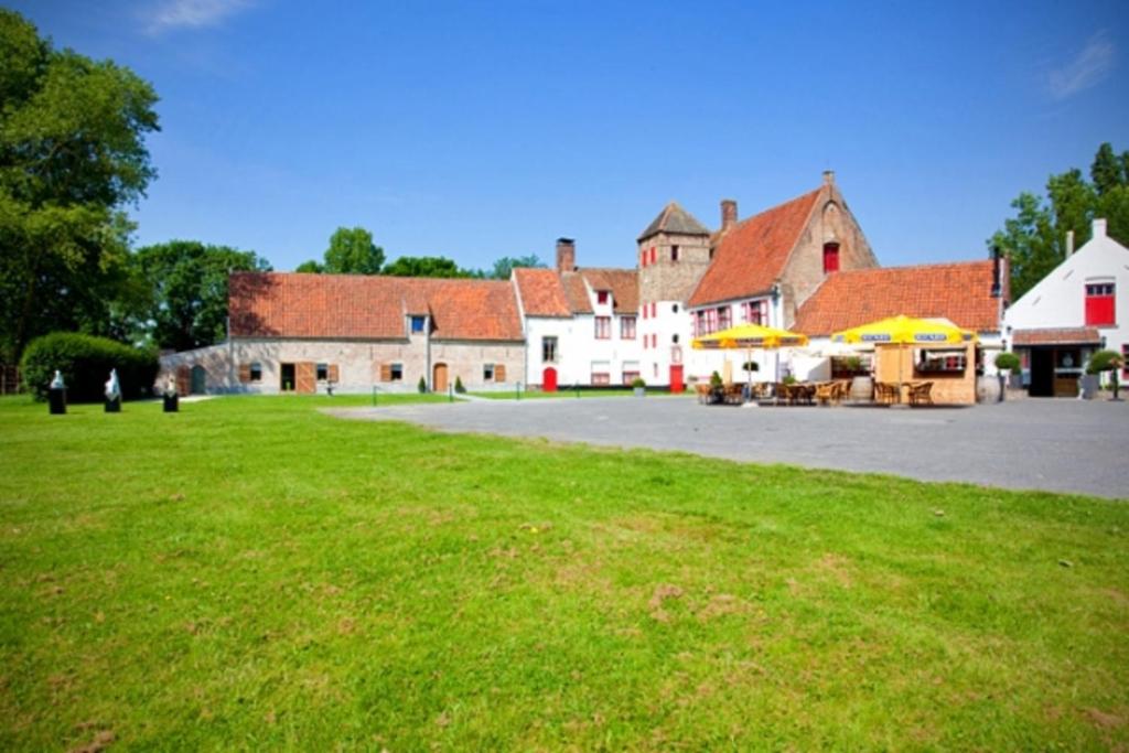 un grand bâtiment avec un champ vert en face dans l'établissement Hostellerie Hof Ter Doest, à Lissewege