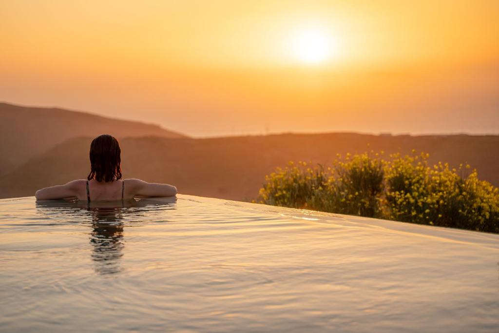 Una donna seduta in una piscina a sfioro a guardare il tramonto di Agrikea a Korissía